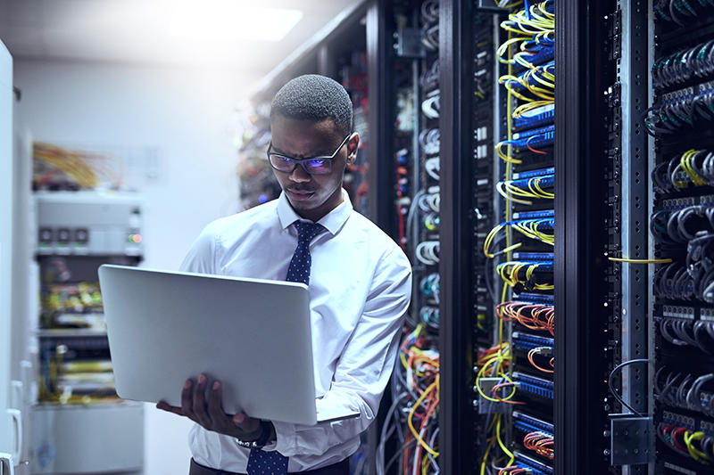 man standing in a computer server room holding a laptop in his arms